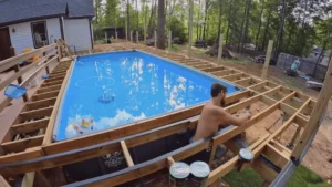 Man building a wooden pool deck around an above-ground pool in a forested backyard – Learn more about the costs and process of building your own pool deck today!