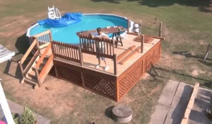 A person constructing a wooden deck around an above-ground pool, ensuring safety and functionality. Build your dream pool deck with expert craftsmanship today!