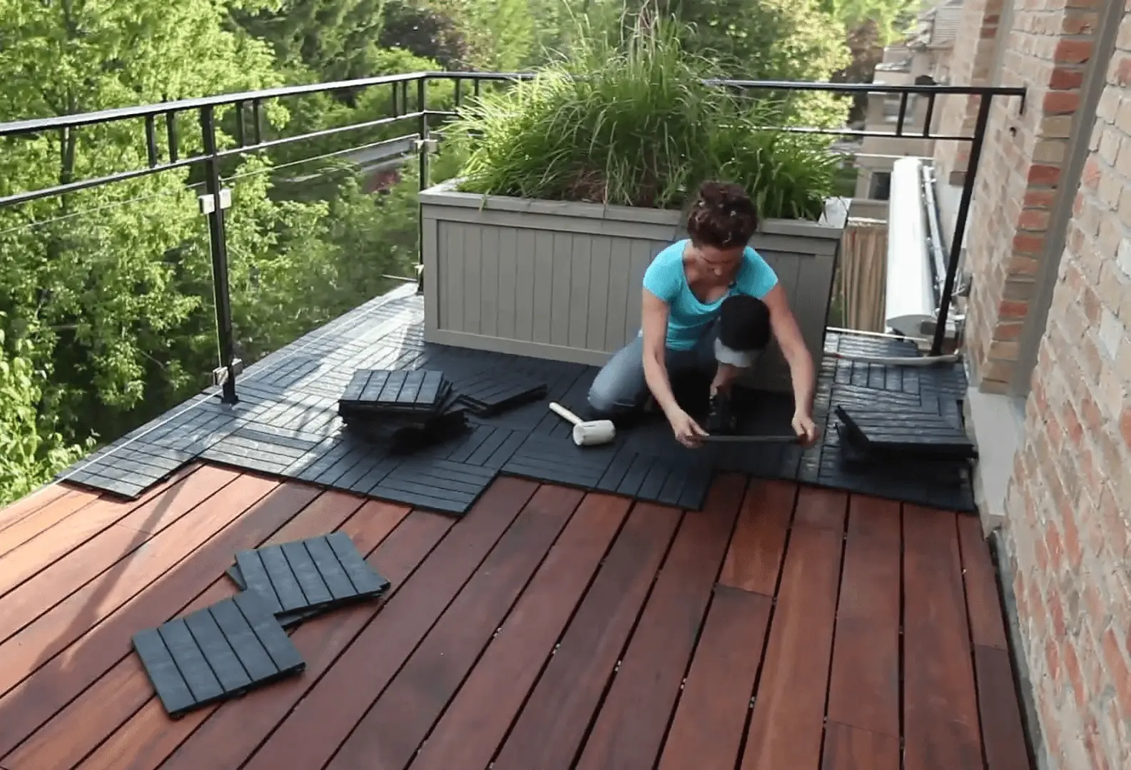 A homeowner installs deck tiles on a balcony with a rubber mallet and a stack of tiles nearby. Hire a professional contractor to ensure a perfect deck installation for your home.