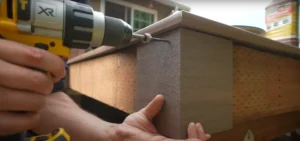 Close-up of a worker using a power drill to secure composite decking boards with screws, demonstrating precise edge finishing.