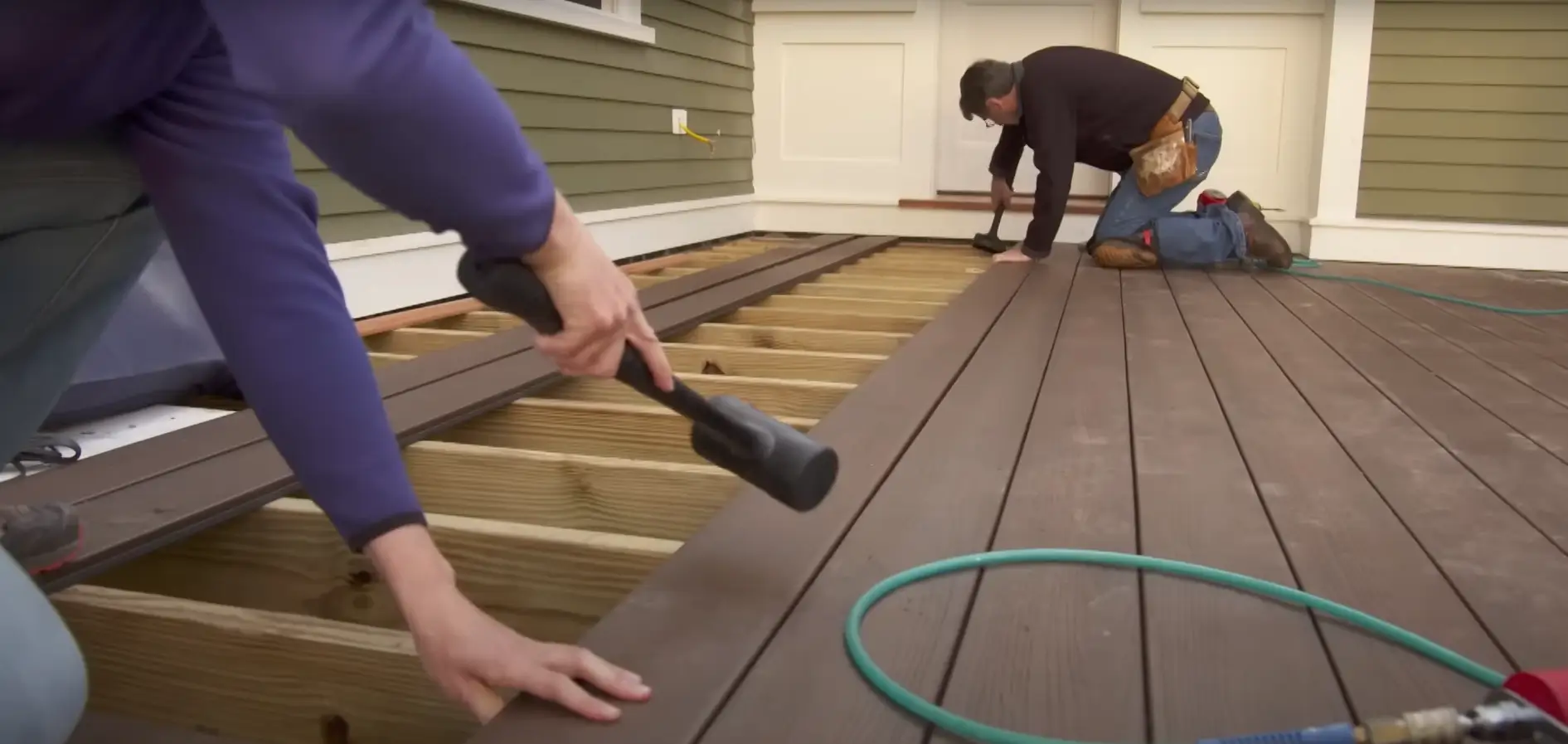 Close-up of workers installing composite decking boards on a wooden frame, using mallets and precision tools to secure the boards.